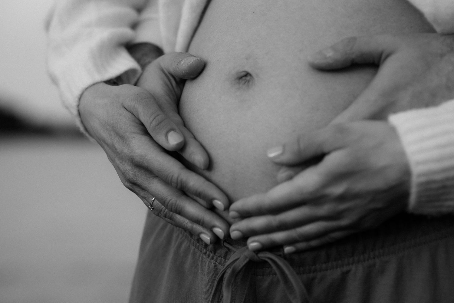 Black and white photo of a pregnant woman with two pairs of hands cradling her baby bump tenderly.