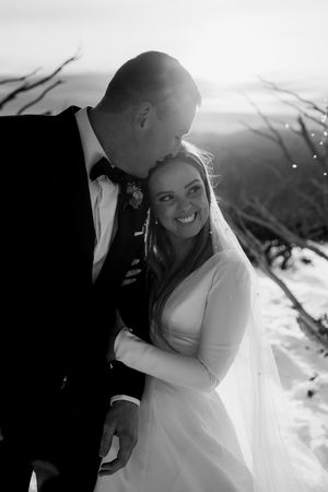 Black and white photo of groom kissing bride on head during romantic winter mountain wedding.