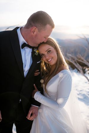Bride smiles warmly as groom kisses her forehead during a romantic winter mountain elopement shoot.