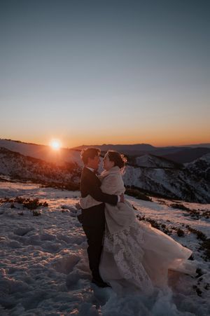 Bride and groom embrace at sunset on a snowy mountain peak, with golden light illuminating their winter wedding elopement.