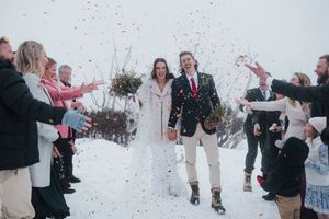 Wedding guests tossing confetti over joyful bride and groom walking through snow during winter outdoor ceremony.