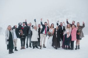 Wedding party celebrating in snowy winter landscape, guests cheering with arms raised around bride and groom.