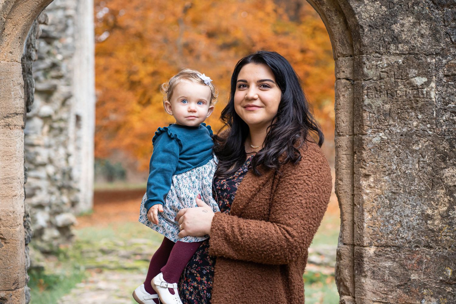 Family of three enjoying autumn outdoors, parents smiling at toddler daughter in colorful fall forest setting.