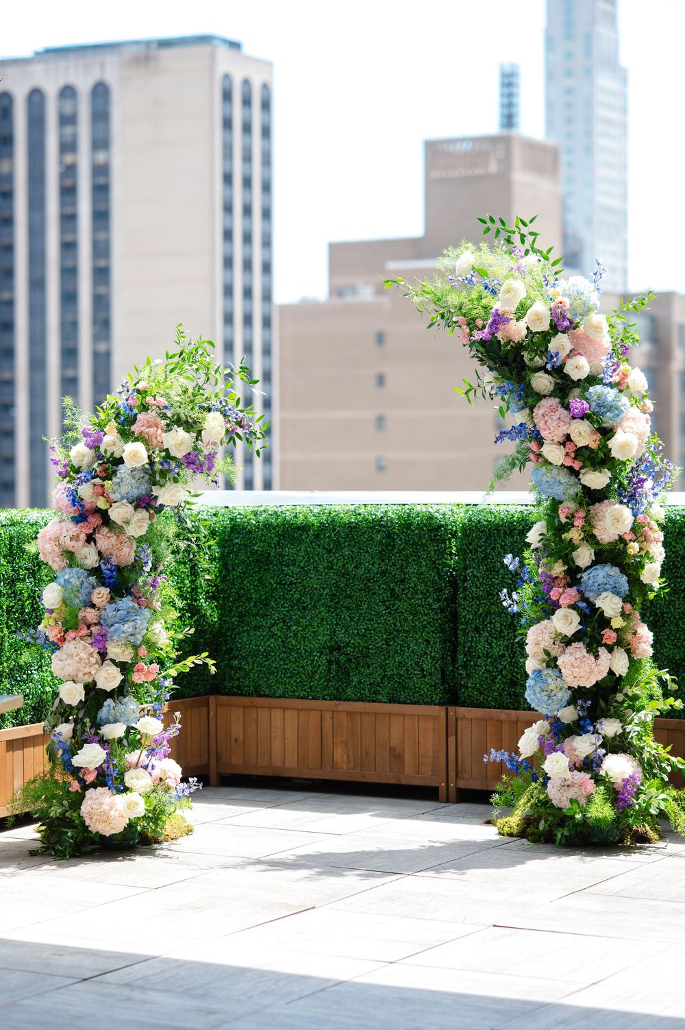 Elegant floral wedding arch with pink, white, and blue blooms on a rooftop with NYC skyline backdrop.