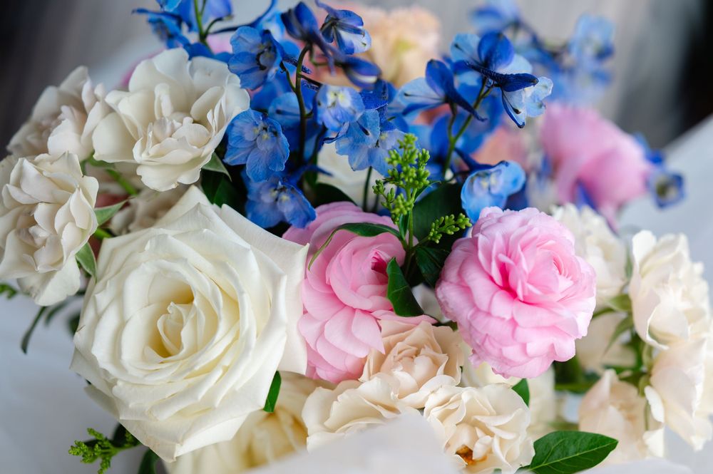 Beautiful floral arrangement featuring white roses, pink camellias, and blue delphiniums.