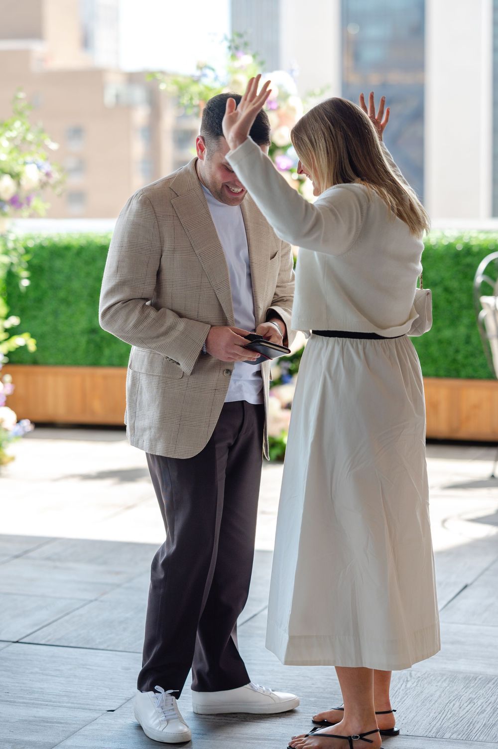 Couple sharing a joyful moment outdoors, woman raising hands in surprise while man holds a phone.