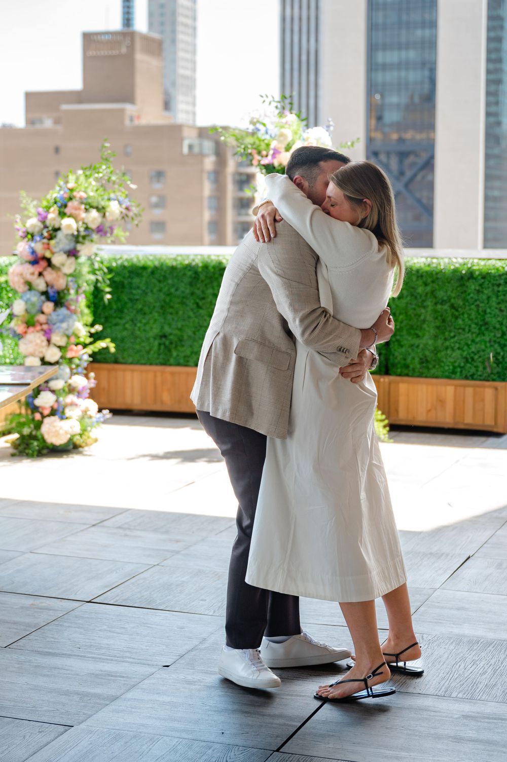 Couple sharing a heartfelt hug during a rooftop proposal with colorful floral arrangements in NYC.
