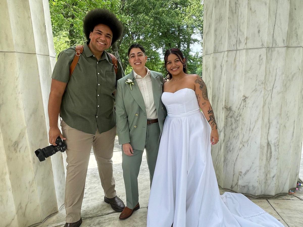Two brides pose with their wedding photographer at the Washington DC War Memorial venue on their special day.