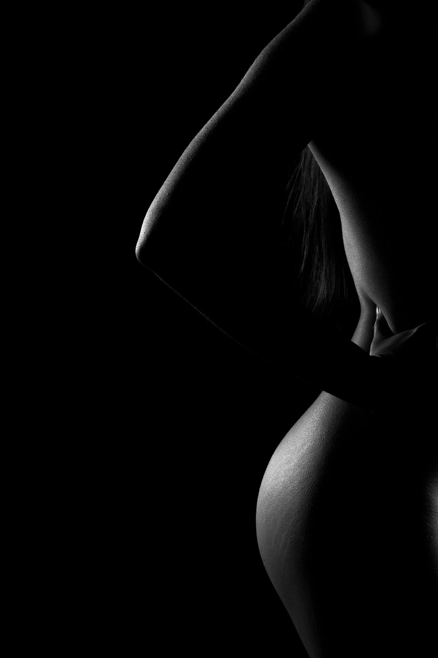 Clarooscuro de silueta boudoir en blanco y negro. Fotografía artística de curvas femeninas con luz de recorte y fondo negro.
