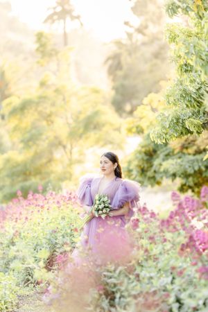 Ethereal photoshoot in a garden with pink flowers and a flowing purple dress creating a dreamy atmosphere.