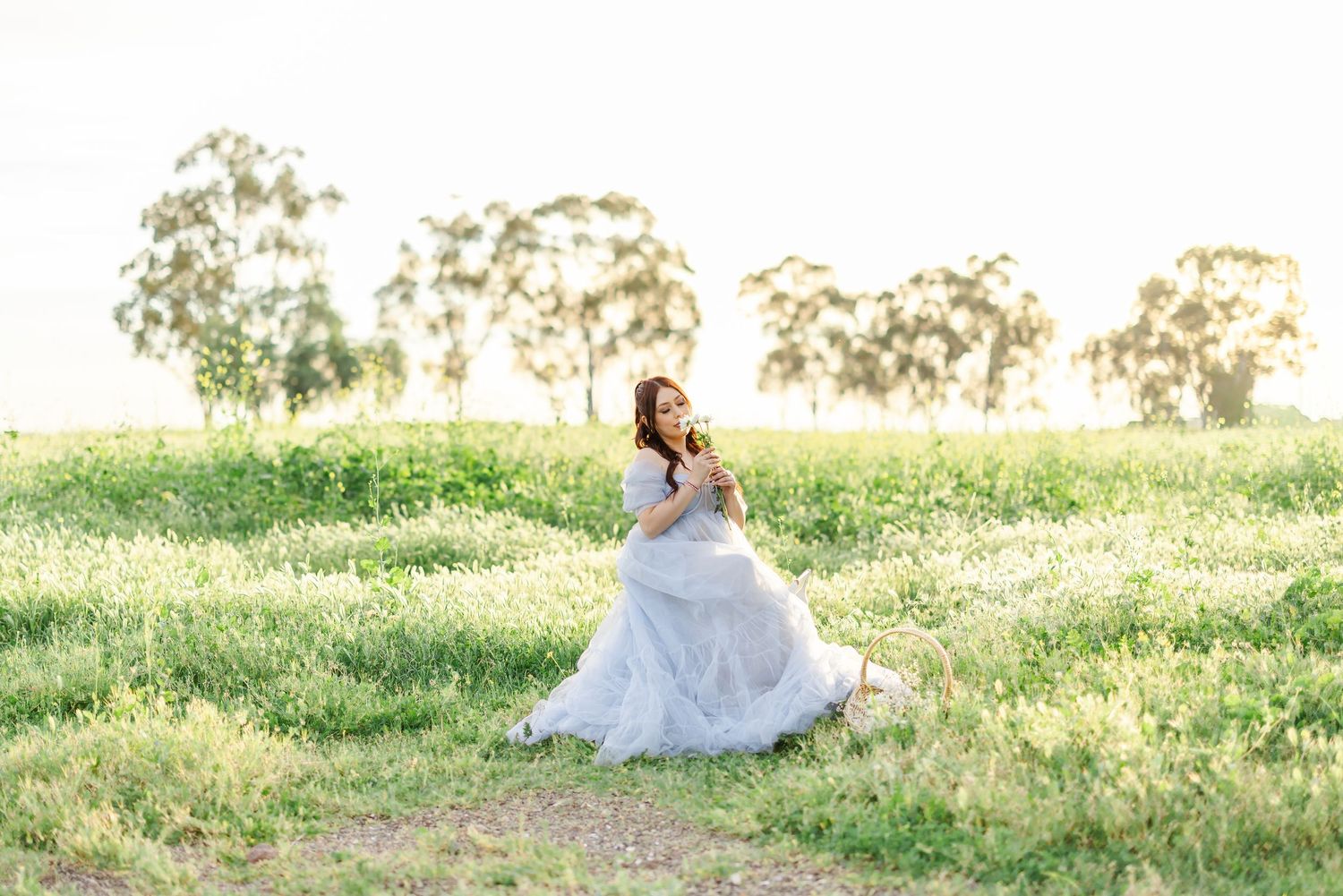 A romantic couple in white attire sits together on a grassy hillside during golden hour.
