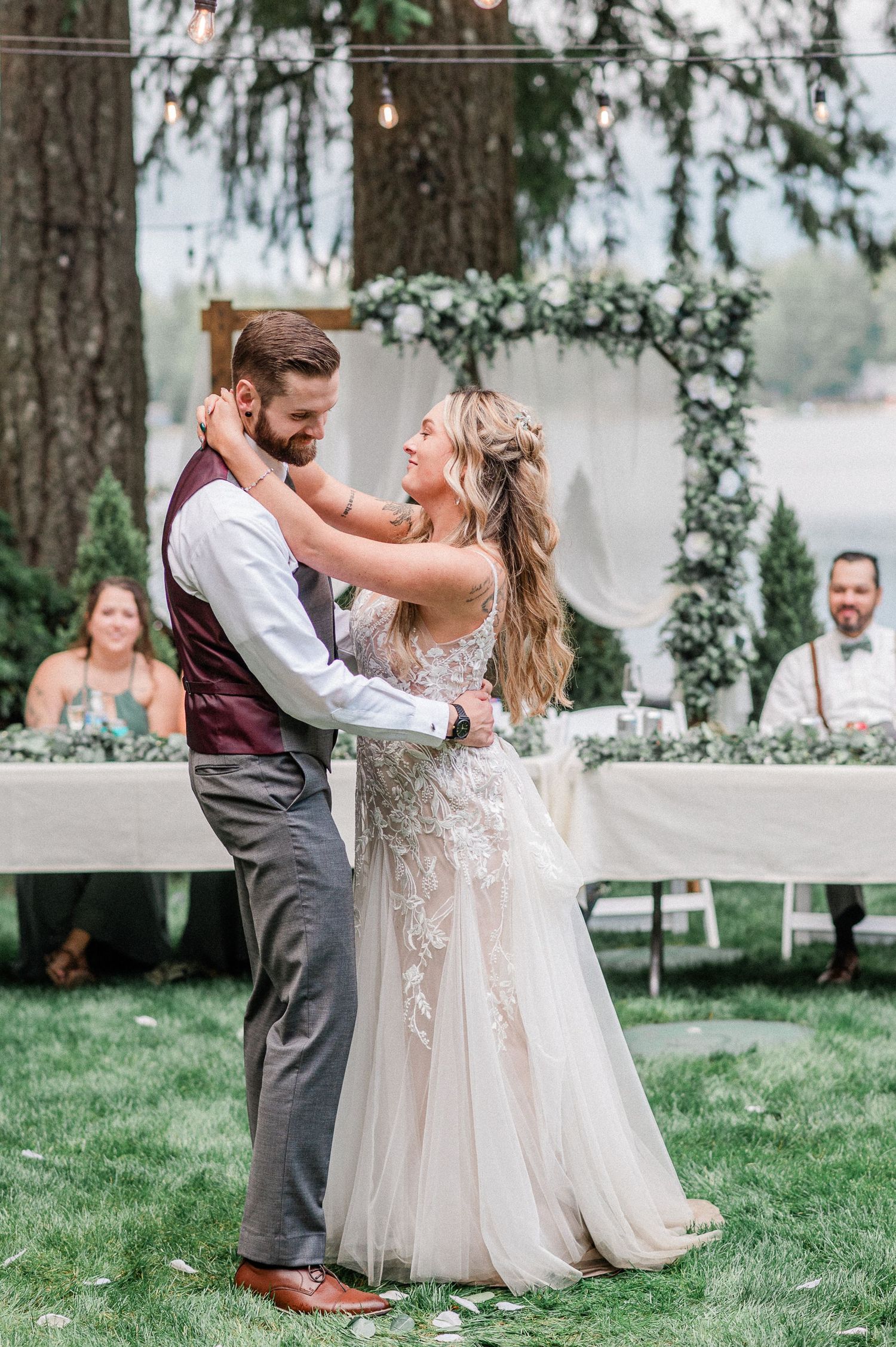 Bride and groom share first dance outdoors at elegant garden wedding with floral arch and string lights.