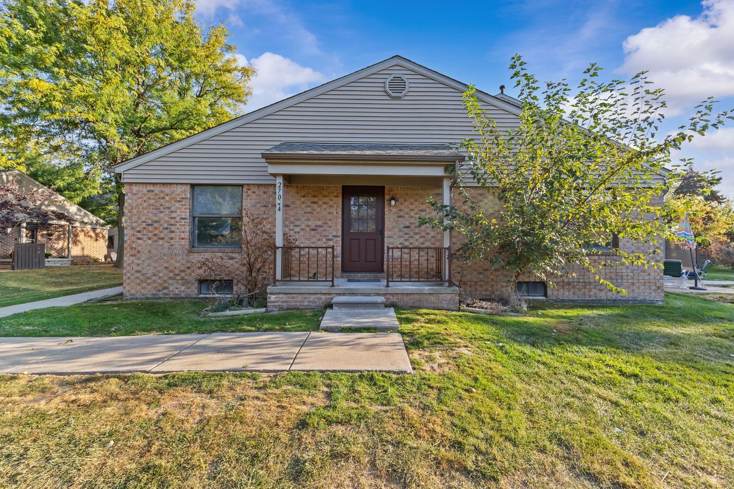 Brick ranch home with covered front porch, green lawn, and mature shade trees lining the property.