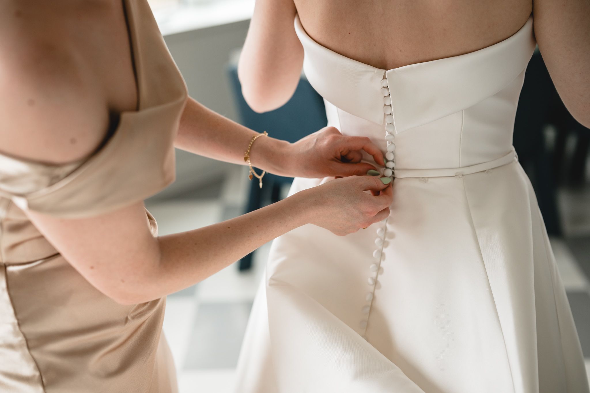 Bridesmaid fastening pearl buttons on the back of a white strapless wedding gown.