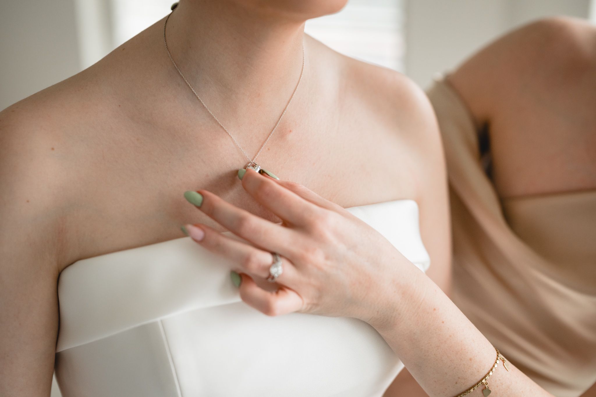 Close-up of bride wearing strapless white gown with delicate gold necklace, diamond ring, and mint green manicure.
