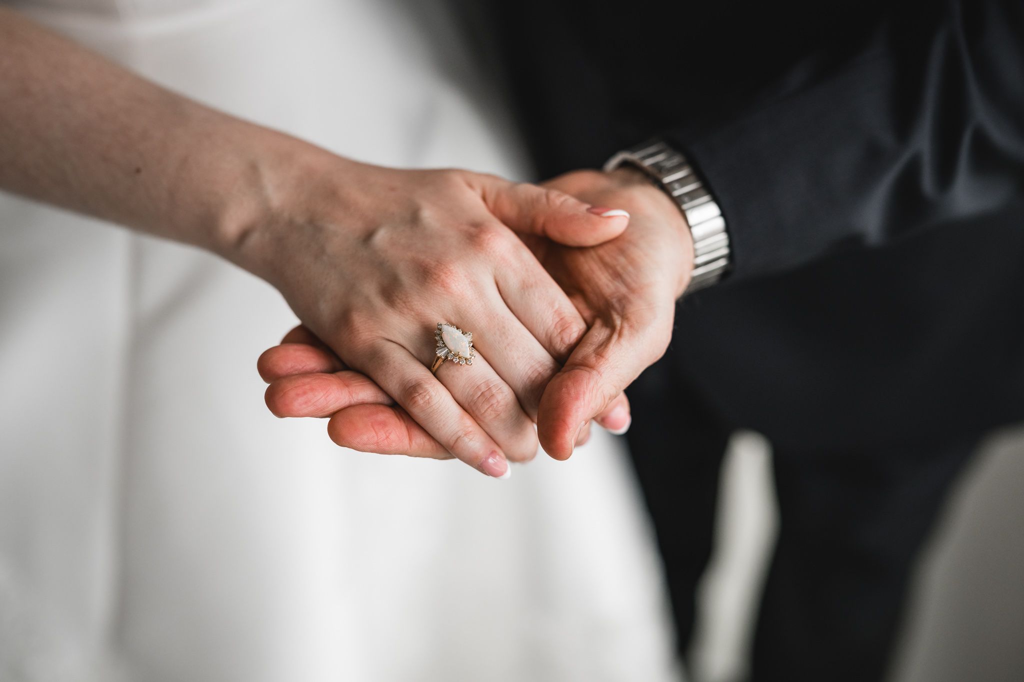 Close-up of bride and groom holding hands, showcasing diamond engagement ring and groom's watch.