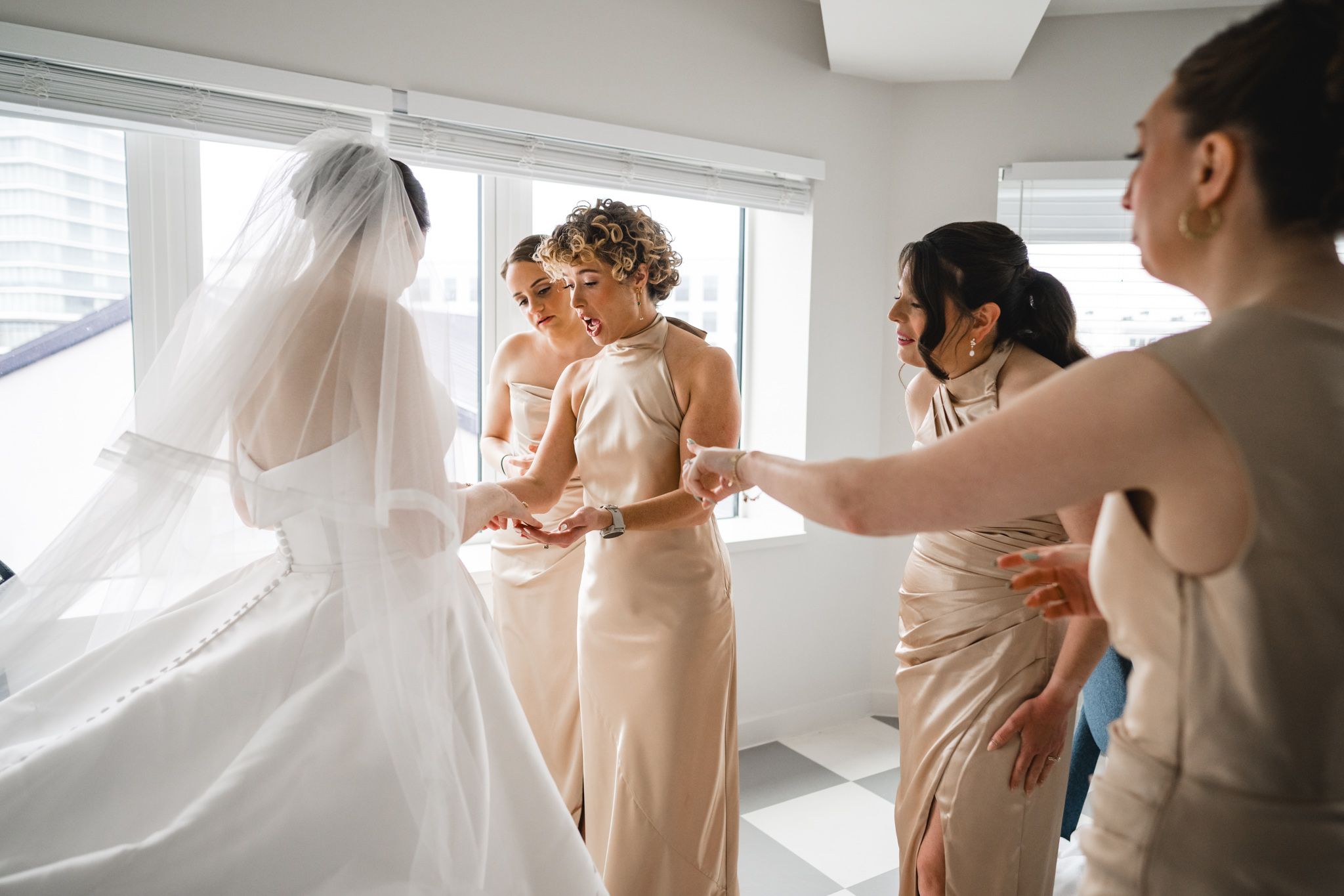 Bridesmaids in champagne gowns helping bride with her white wedding dress and veil before ceremony.