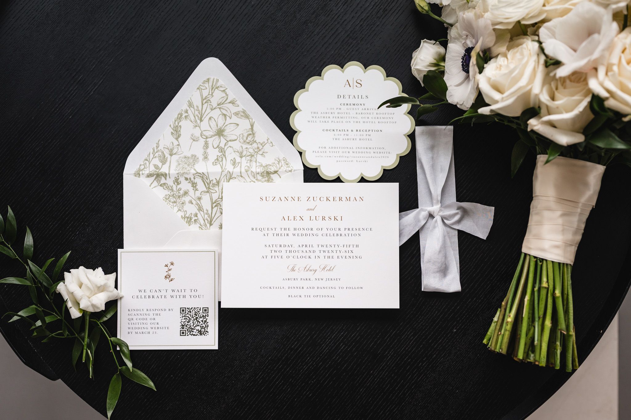 Elegant wedding invitation suite with floral envelope liner, scalloped details, white roses bouquet on dark table.