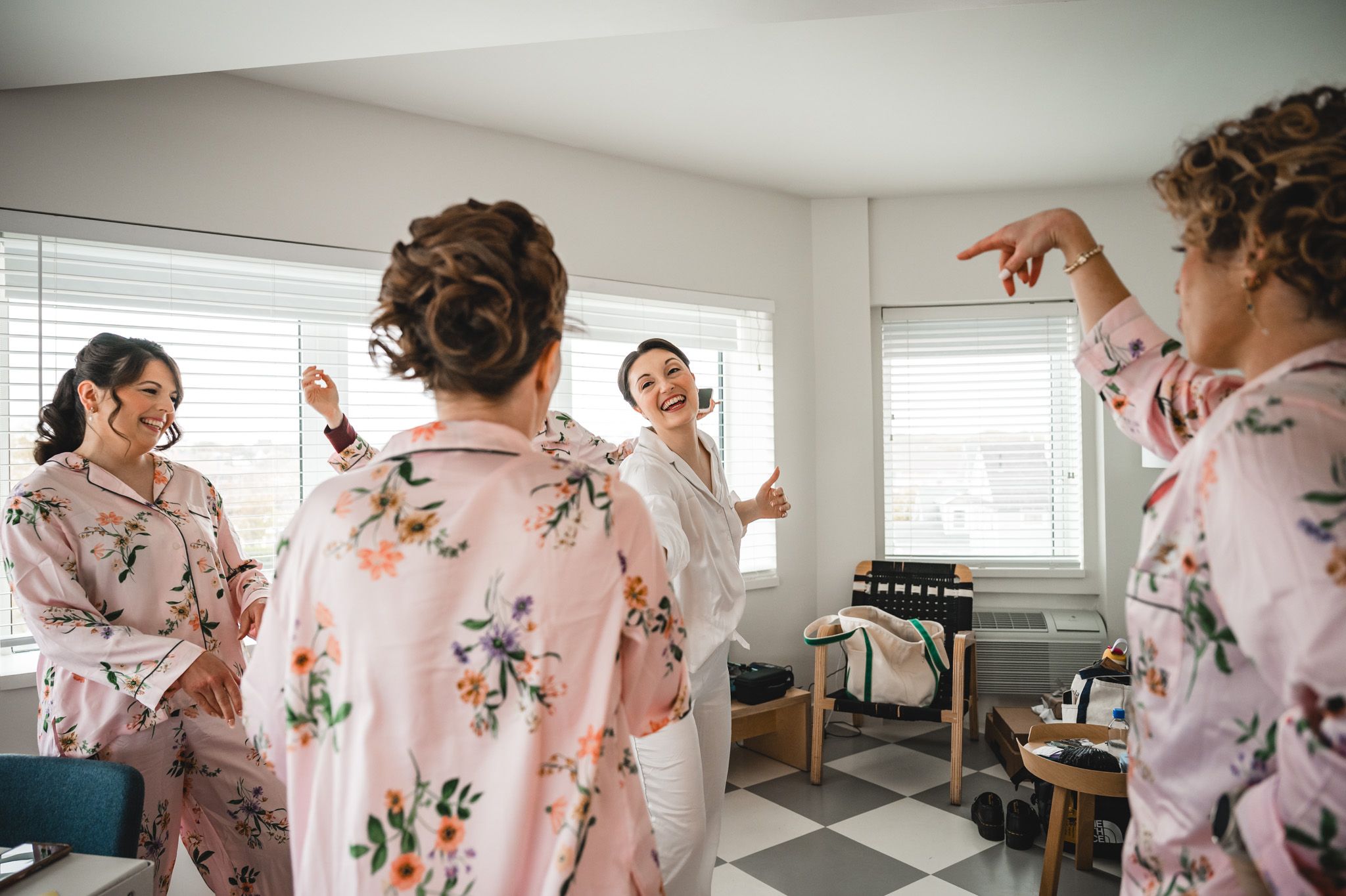 Bridesmaids in matching pink floral robes laughing and celebrating together during wedding morning preparations.