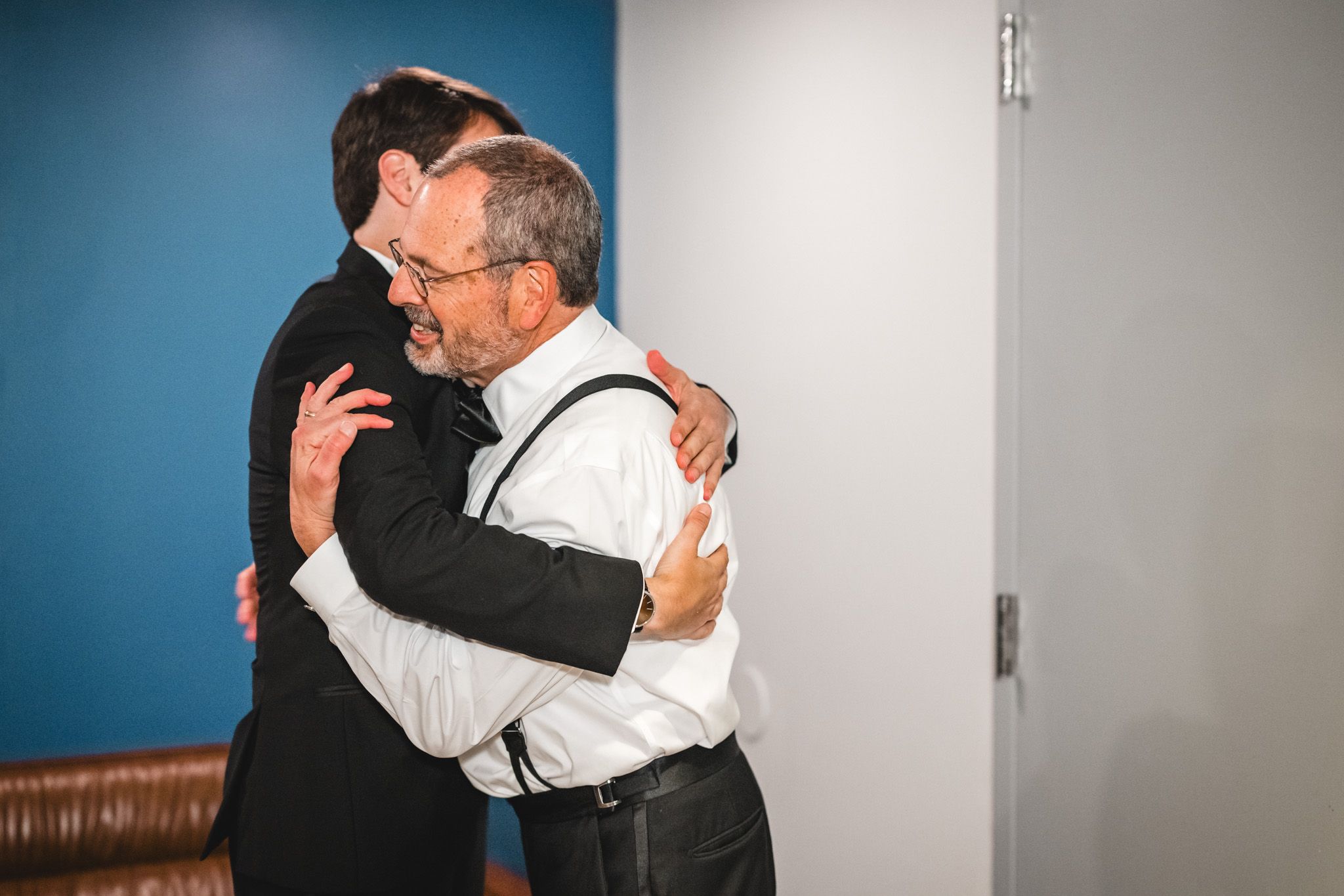 Two men sharing a warm emotional hug during wedding day celebrations in a modern venue.
