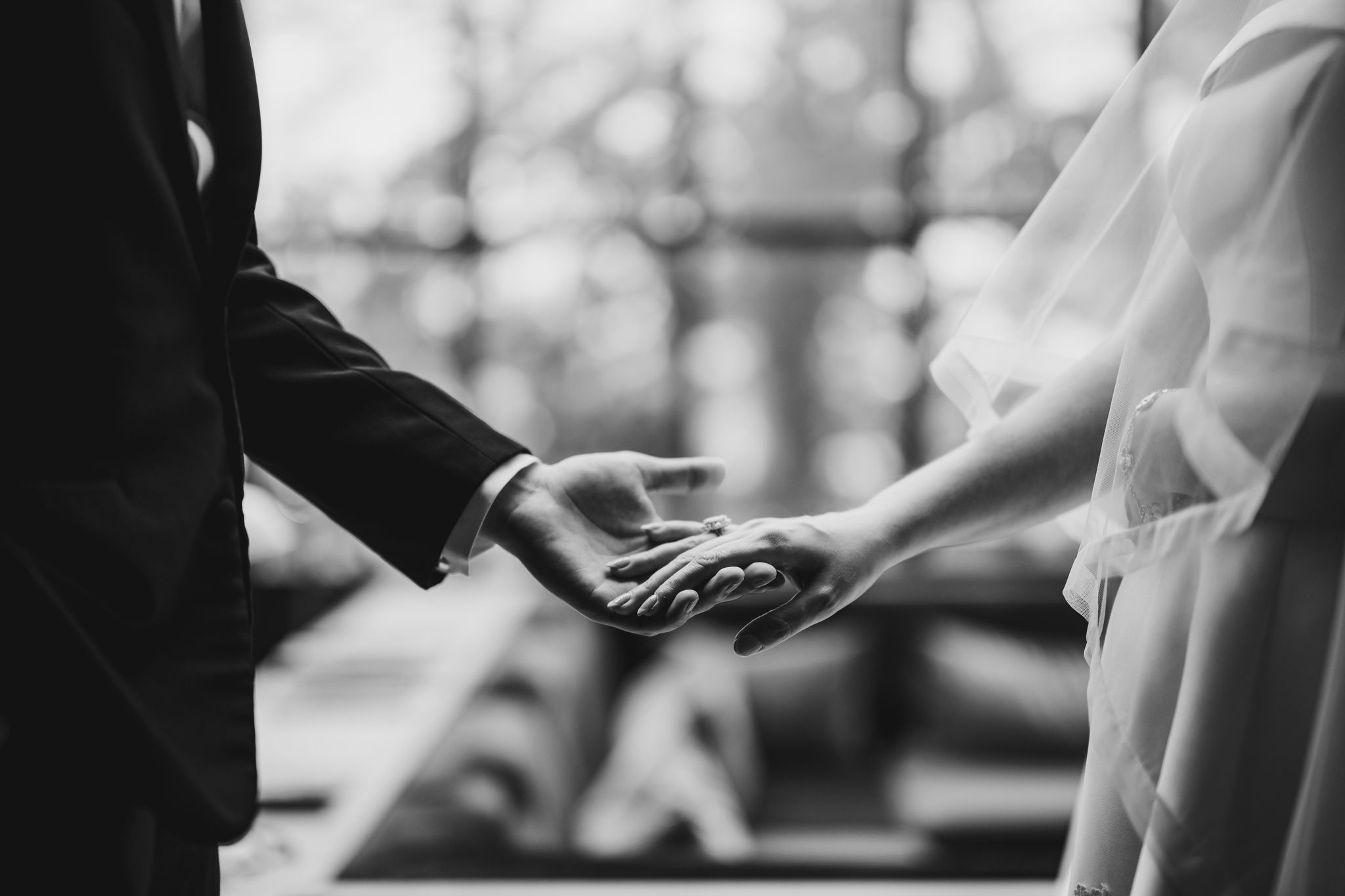 Black and white photo of bride and groom holding hands at wedding ceremony.