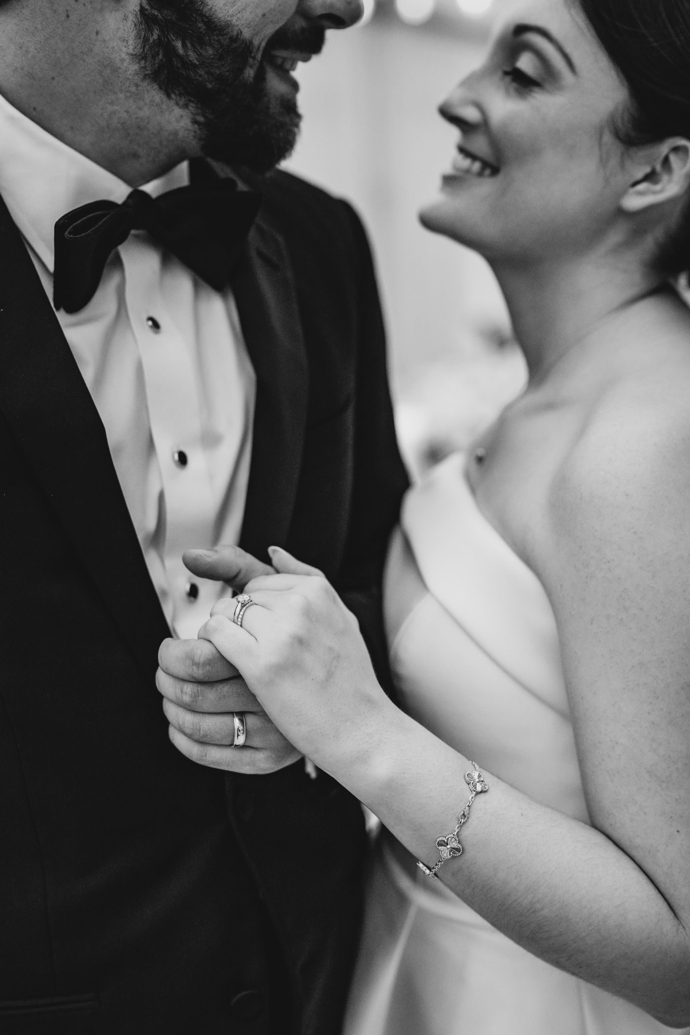 Black and white close-up of bride smiling at groom while holding his hand showing wedding rings.