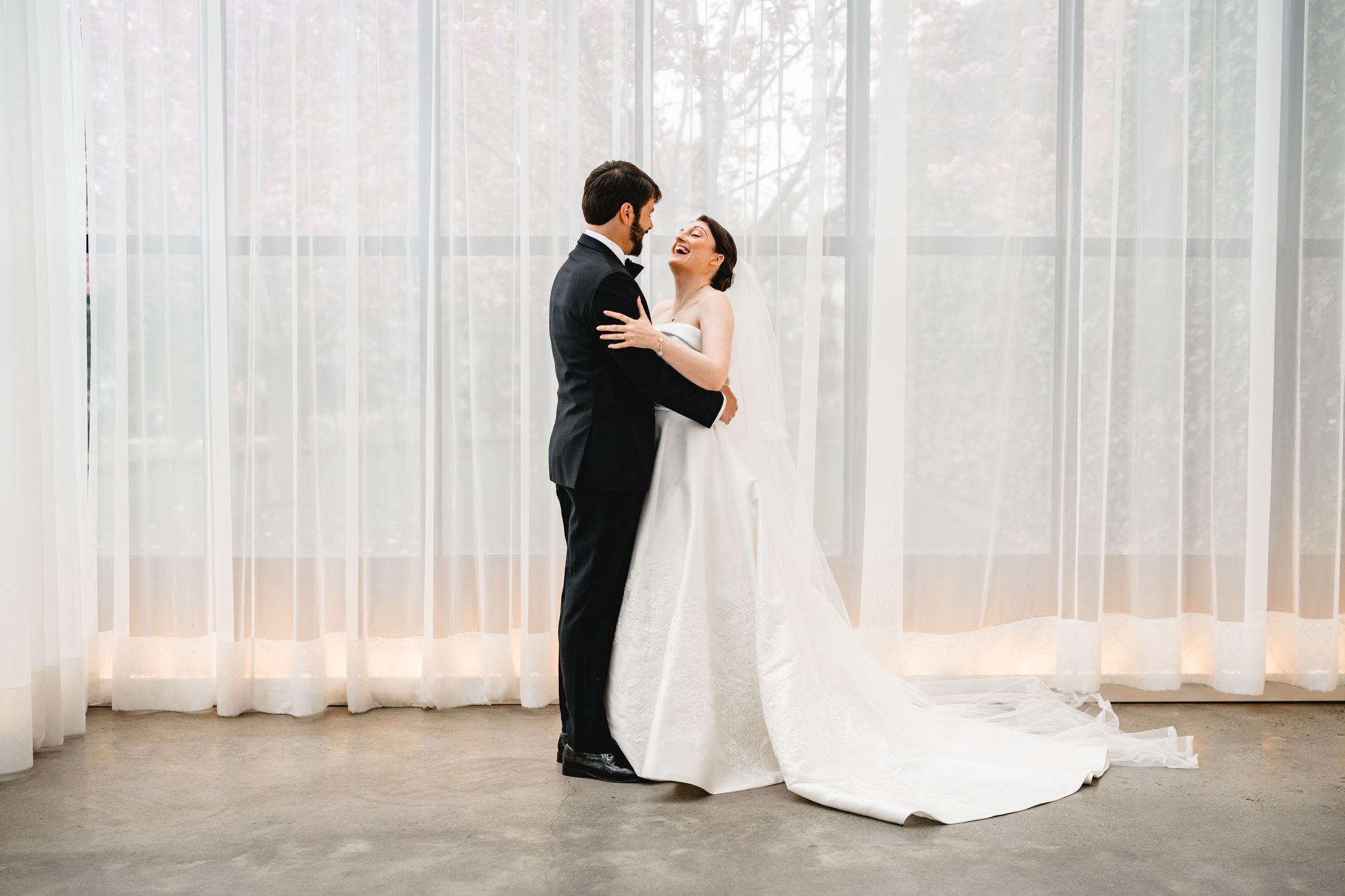 Bride and groom sharing an intimate embrace during first look in front of sheer white curtains.