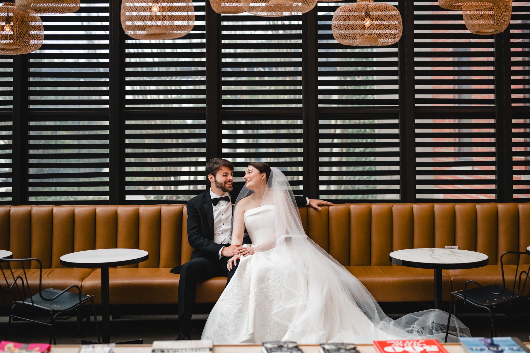 Bride and groom sitting together on leather banquette in elegant restaurant venue after wedding ceremony.