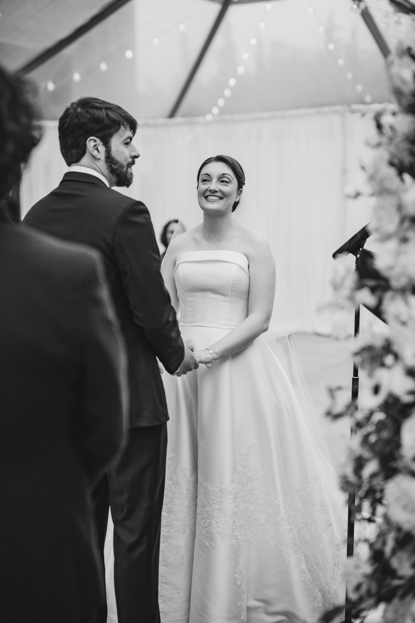 Bride and groom hold hands and exchange vows at their wedding ceremony under a tented venue.