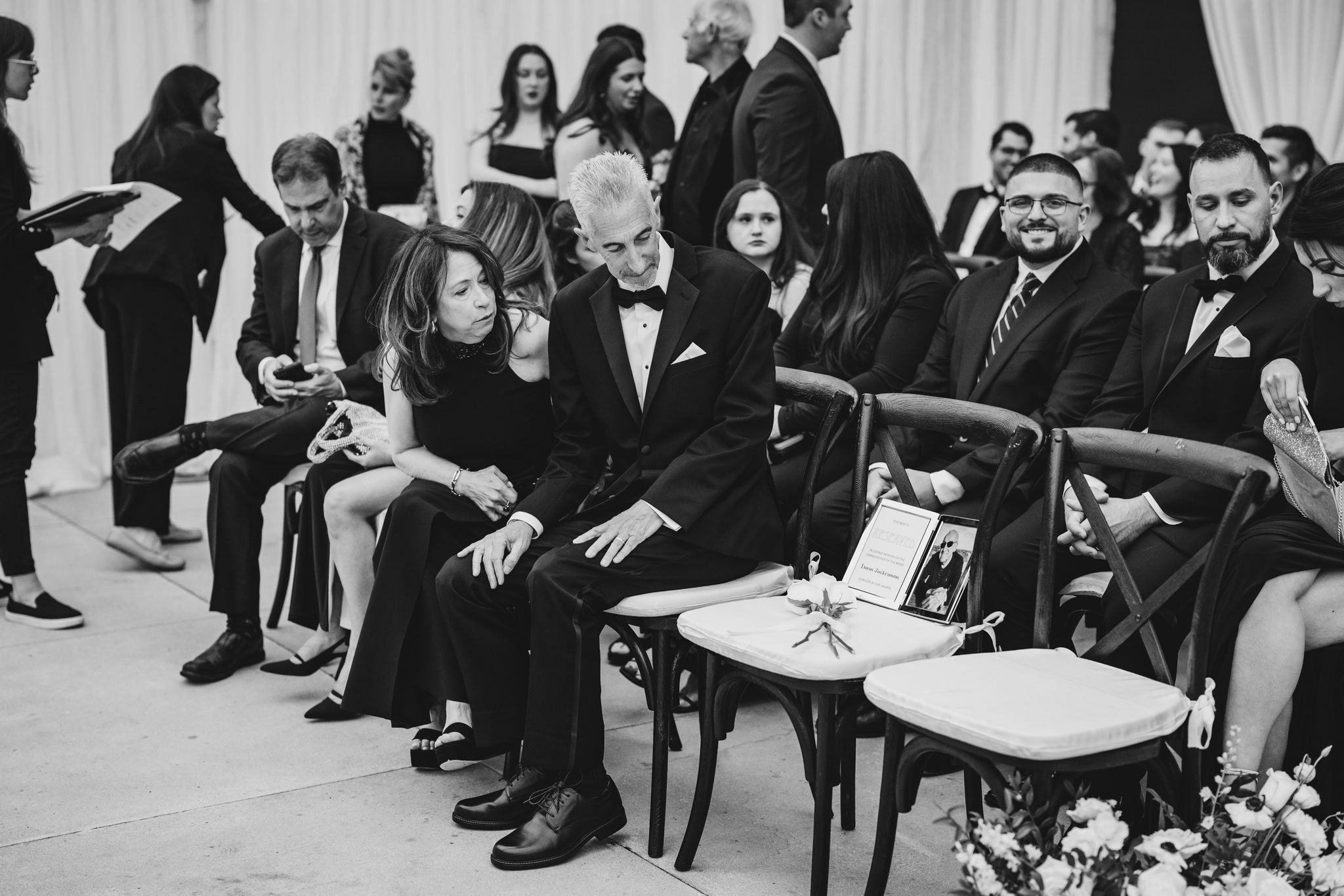 Wedding guests seated during ceremony in black and white photo showing emotional family members in formal attire.