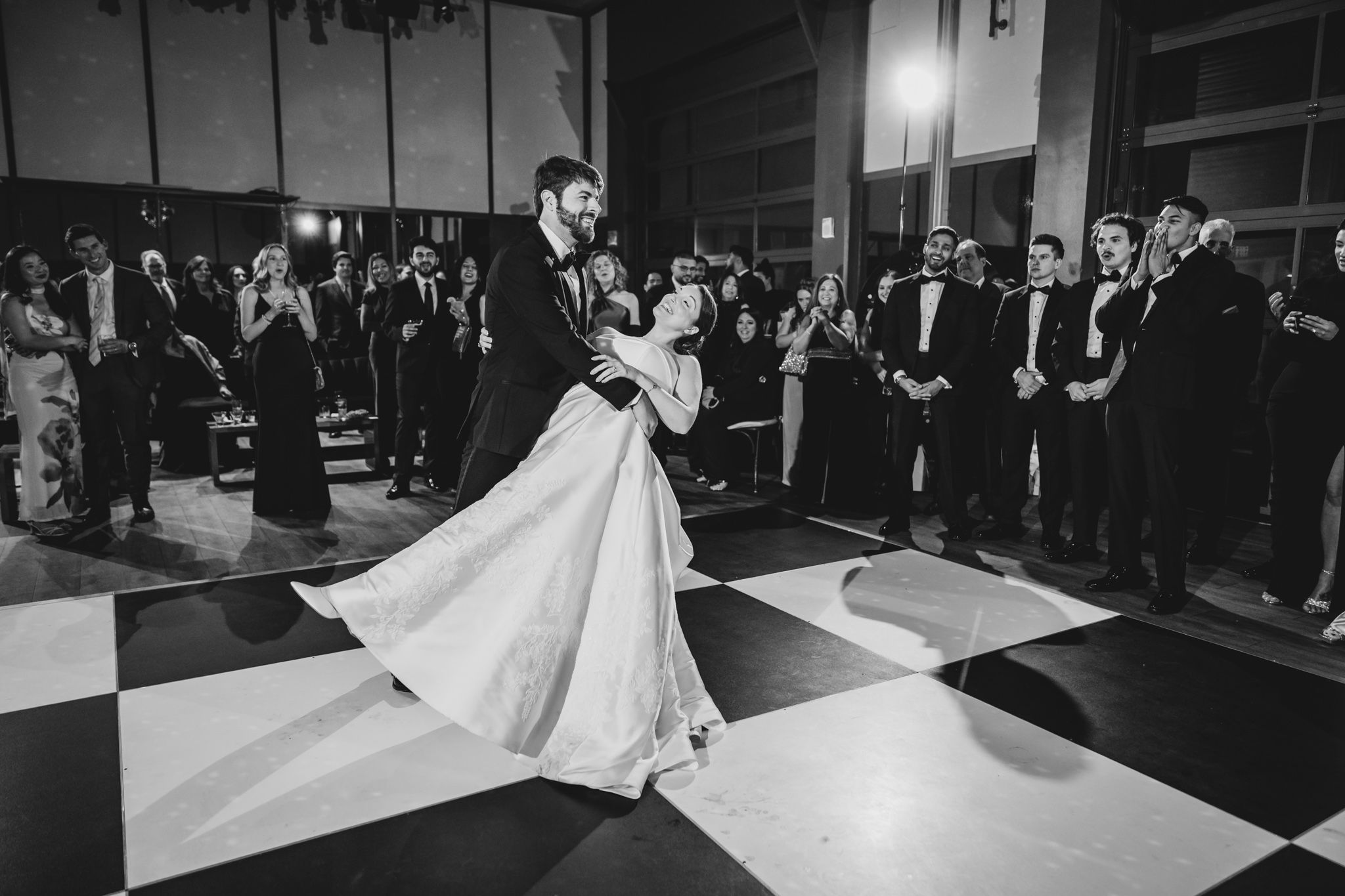 Bride and groom share their first dance on a black and white checkered dance floor at their wedding reception.