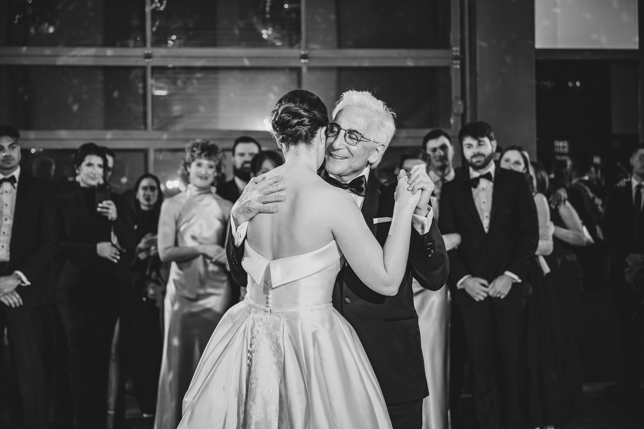 Black and white photo of bride sharing an emotional father-daughter dance at elegant wedding reception.