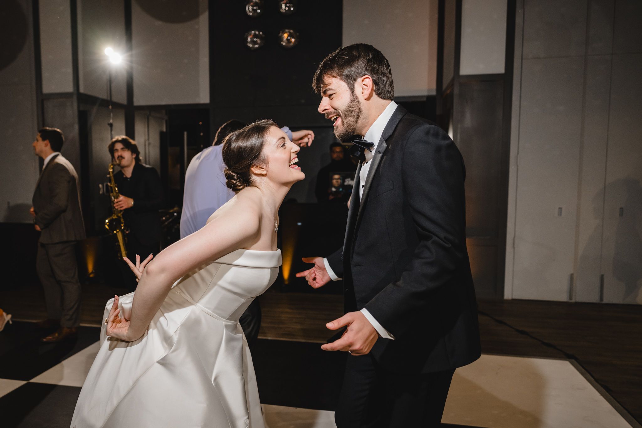 Bride and groom laugh together intimately during their first dance on a black and white checkered floor.