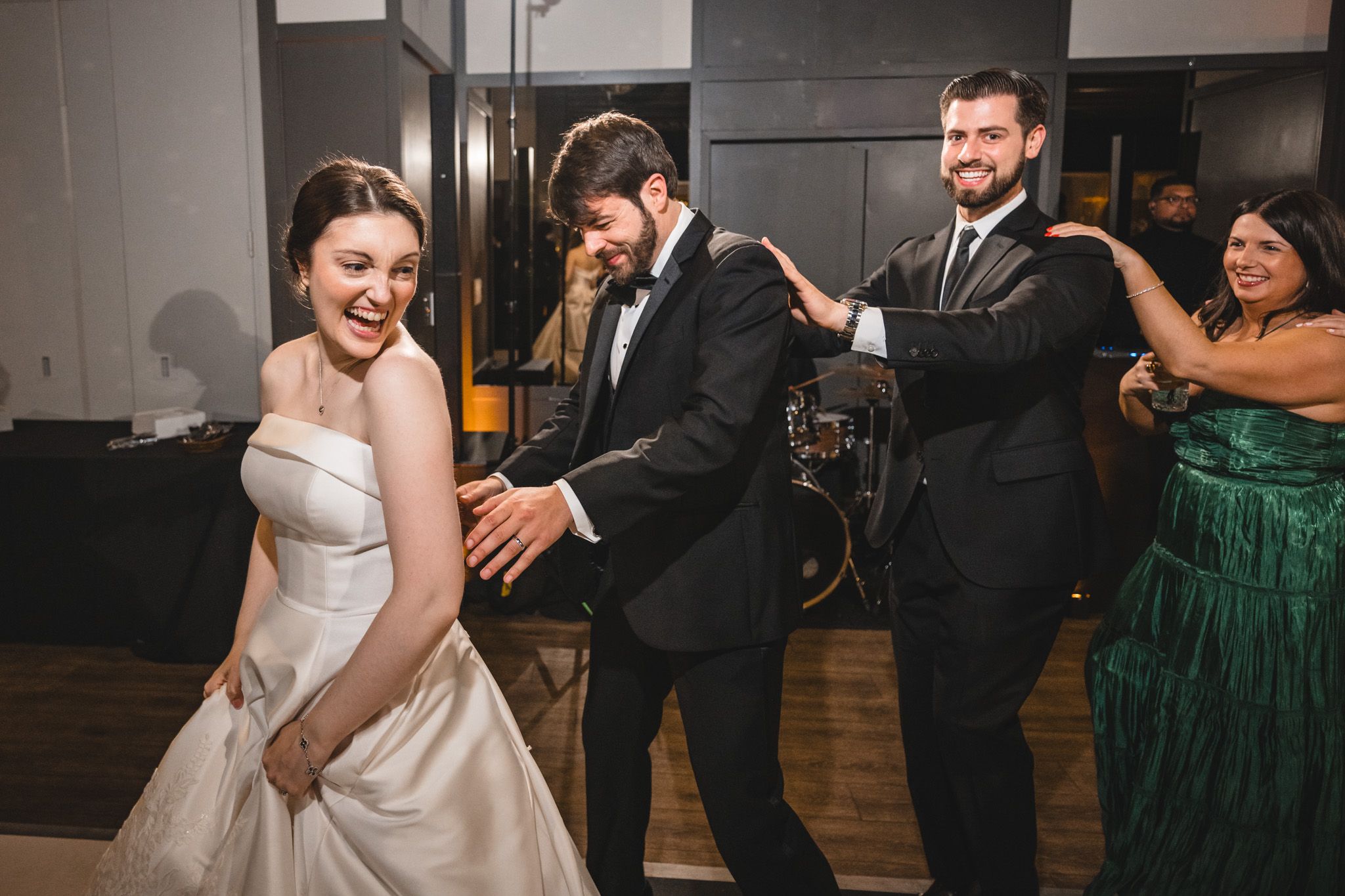 Bride and groom dancing joyfully at wedding reception with guests in formal attire celebrating in background.