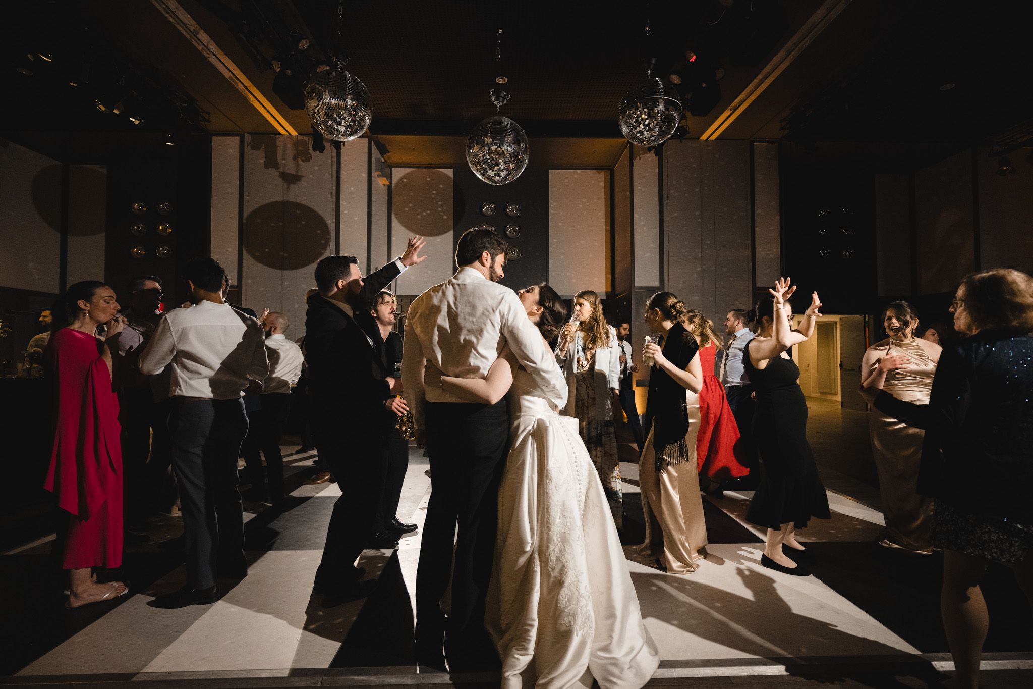 Bride and groom share first dance surrounded by celebrating guests in elegant dimly lit wedding reception venue.