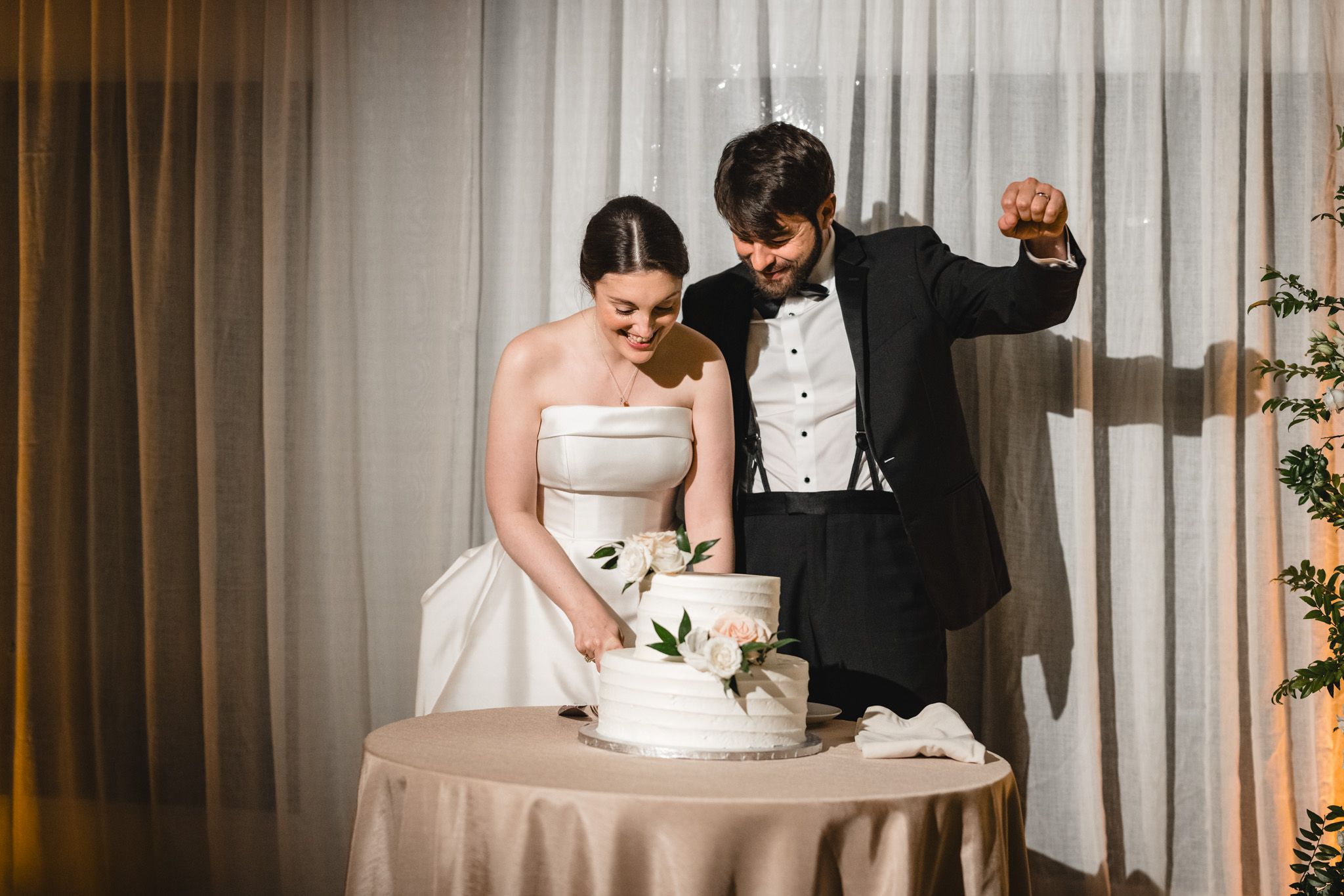 Bride and groom cutting their elegant white wedding cake together at their indoor reception venue.