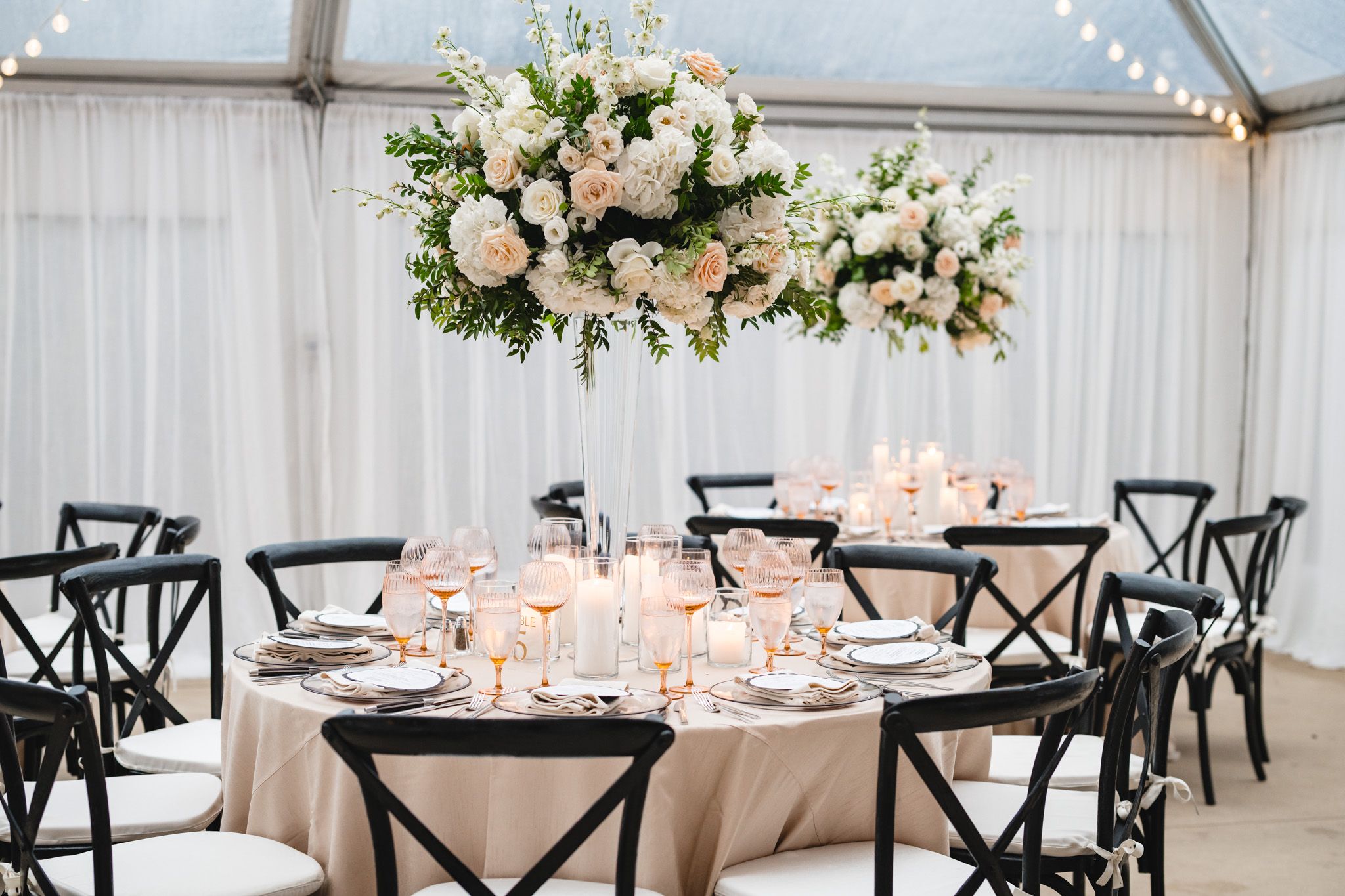 Elegant wedding reception table with black chairs, champagne linens, and a tall white floral centerpiece.