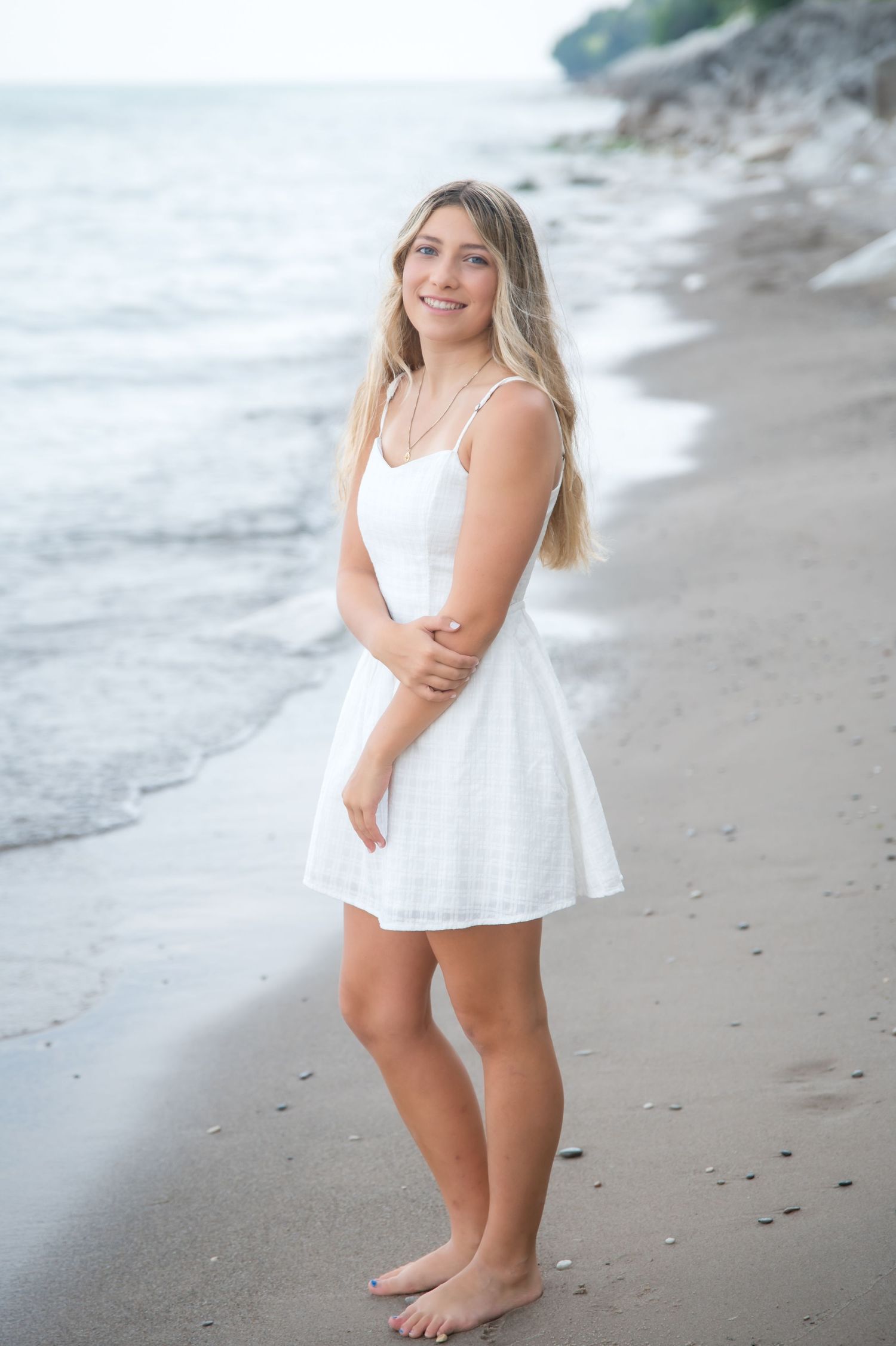 Smiling blonde woman in white crop top and jeans sitting on a concrete pier by the ocean.