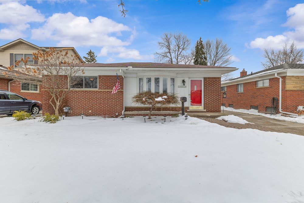 Brick ranch home with red front door and snow-covered yard in winter.