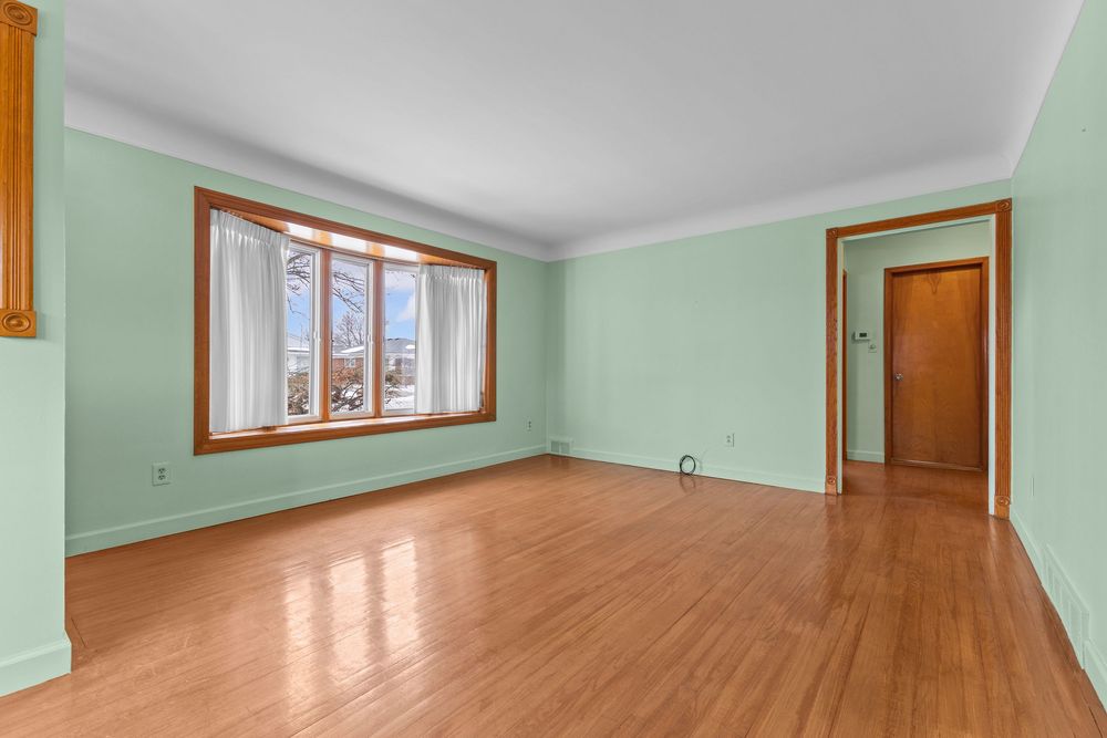 Empty room with light green walls, hardwood floors, a large window, and warm wood trim accents.