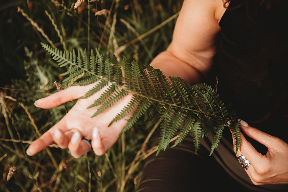 Close-up of a woman holding a green fern leaf in her outstretched hand outdoors in nature.