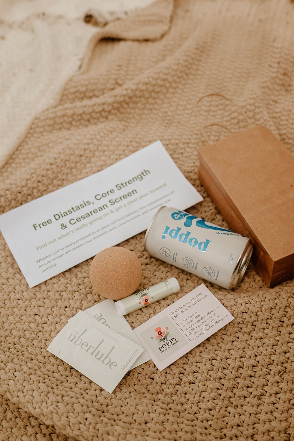 Postpartum recovery kit with Poppi soda, Uberlube, konjac sponge, and free diastasis core strength screening card.
