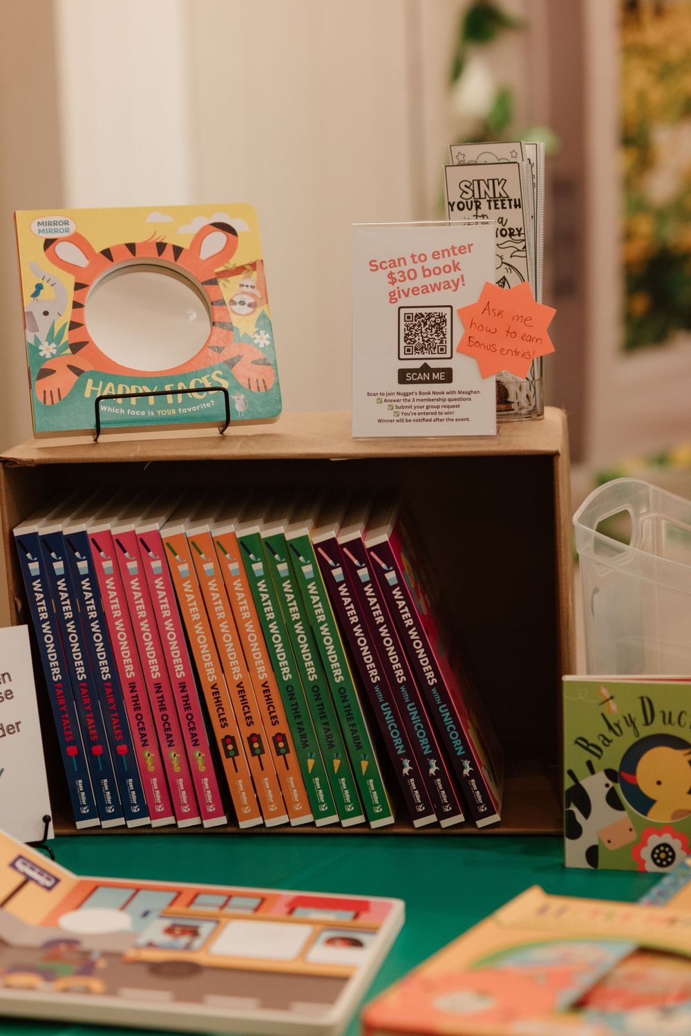 A wooden bookshelf display with colorful children's books and a QR code sign for a $30 book giveaway.