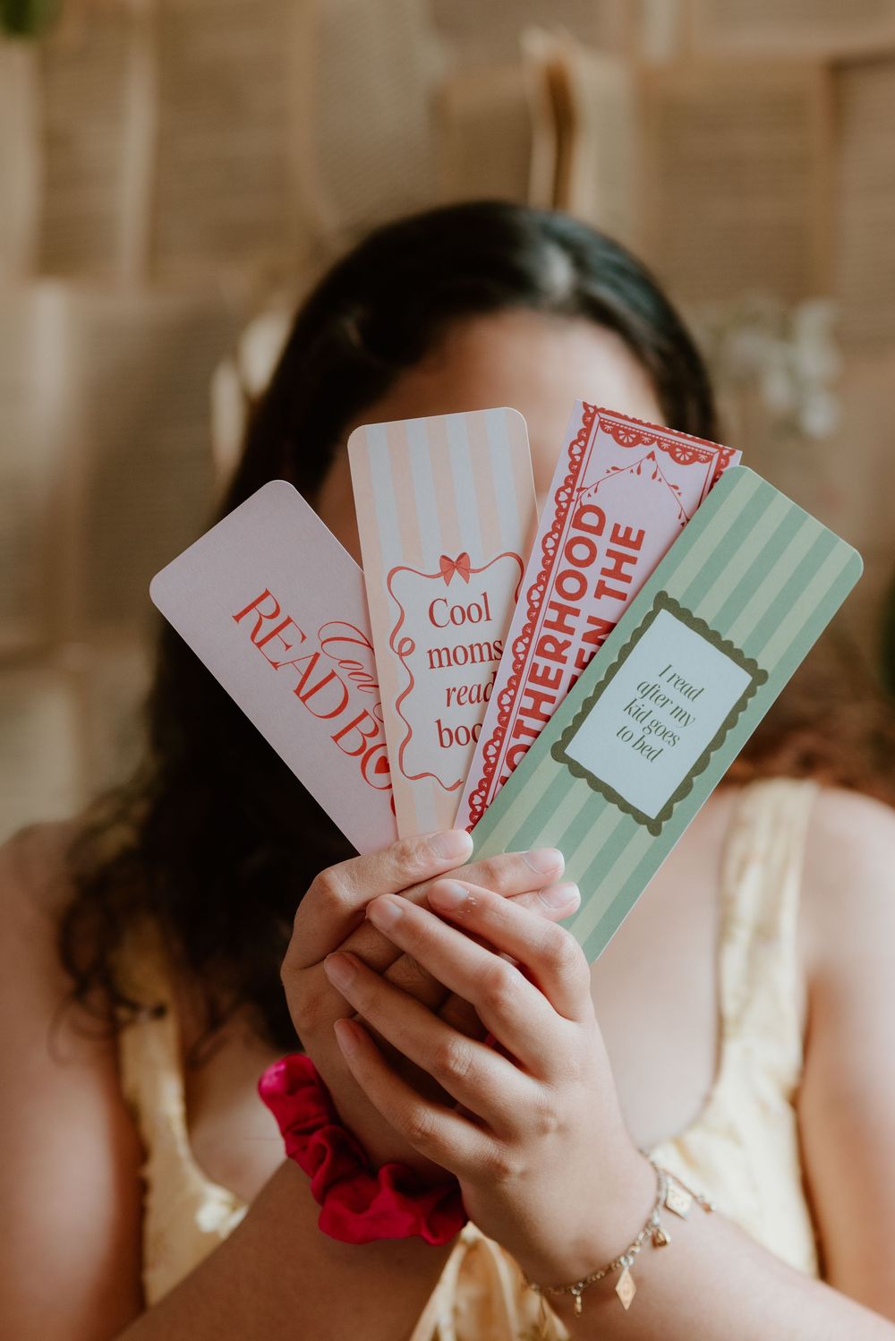 Woman holding four colorful bookmarks with reading-themed quotes, including Cool Moms Read Books and Motherhood.