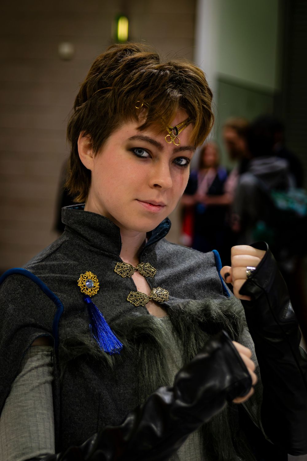 Woman cosplaying in medieval fantasy costume with gold brooch, fur trim, and ornate headpiece at a convention.