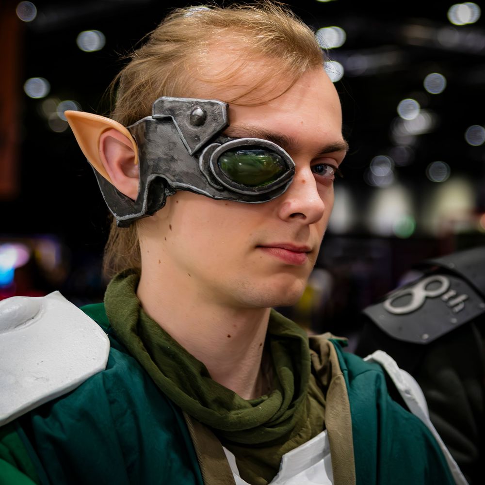 Young cosplayer wearing elf ears and steampunk goggles at a gaming convention.