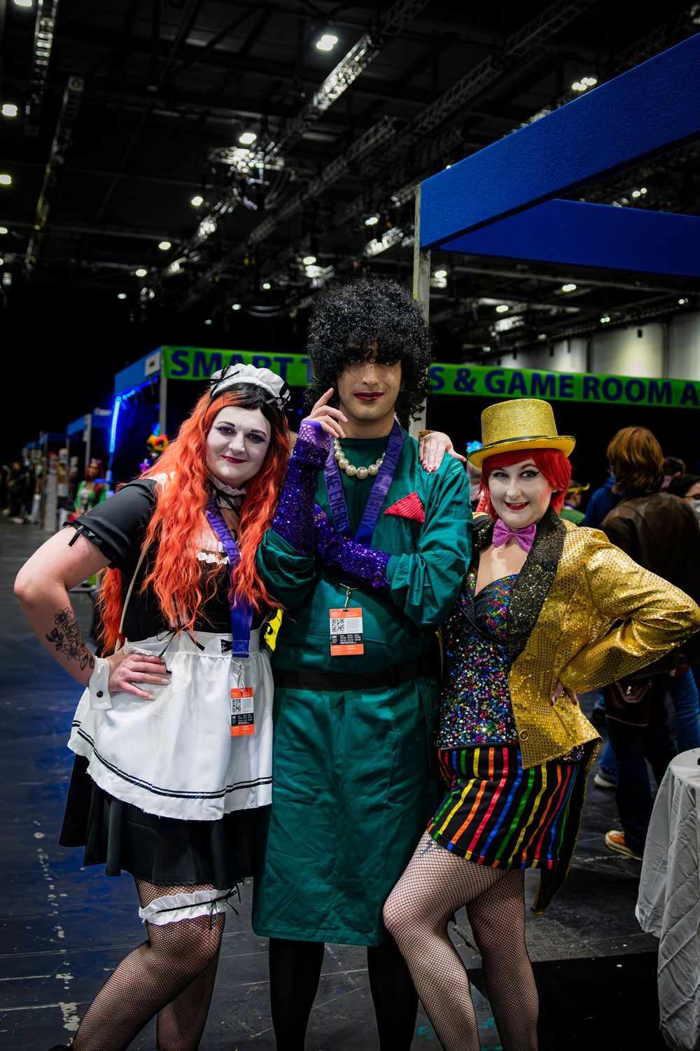 Three cosplayers in colorful costumes pose together at a gaming convention hall.
