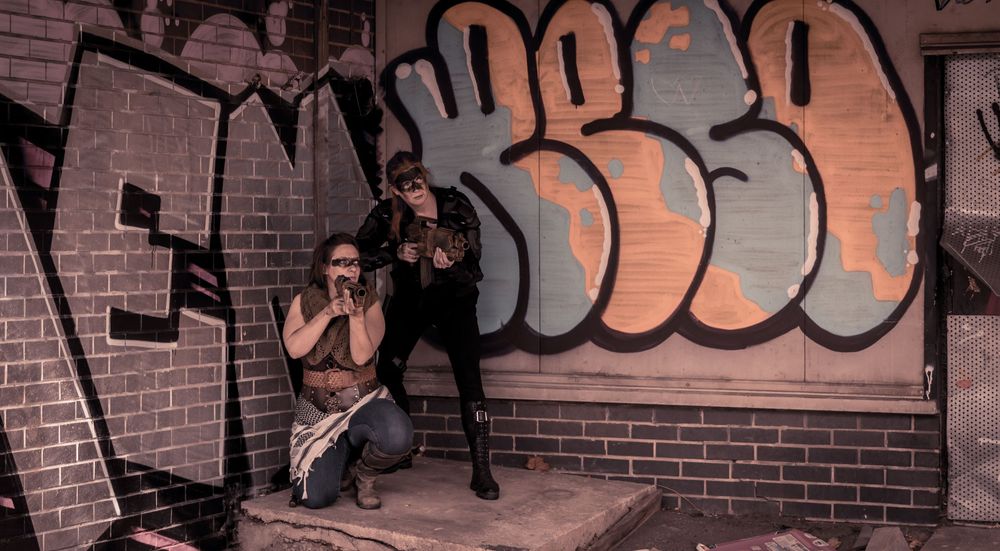 Two people posing in front of colorful graffiti wall art on brick in an urban setting.