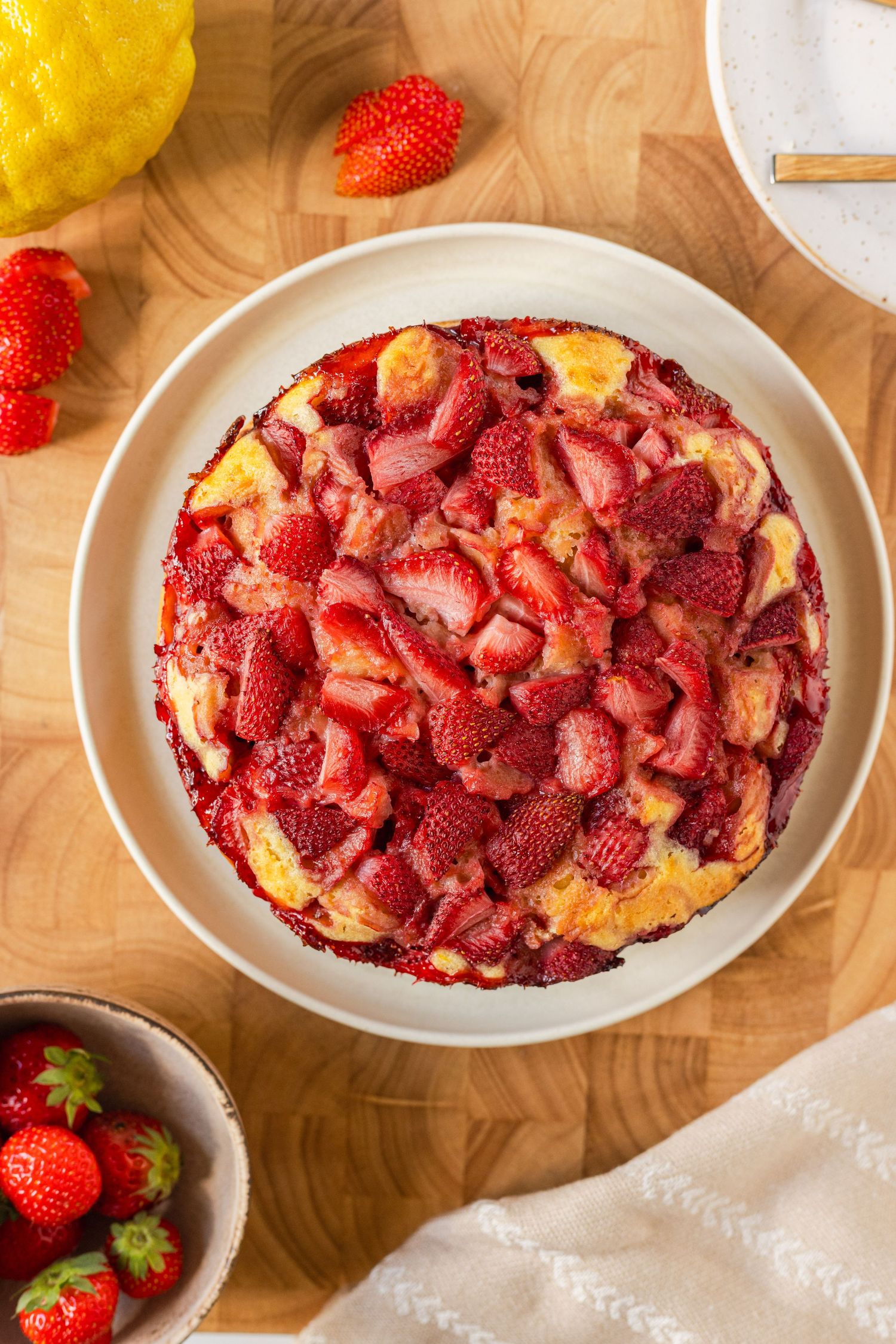 Overhead view of a strawberry upside-down cake on a wooden board, topped with fresh sliced strawberries.