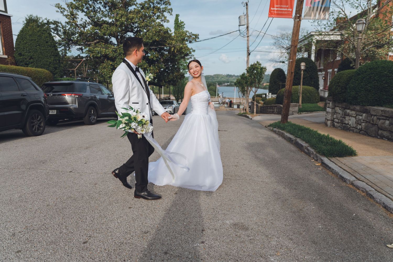 Bride and groom walk hand in hand down a sunny street on their wedding day.